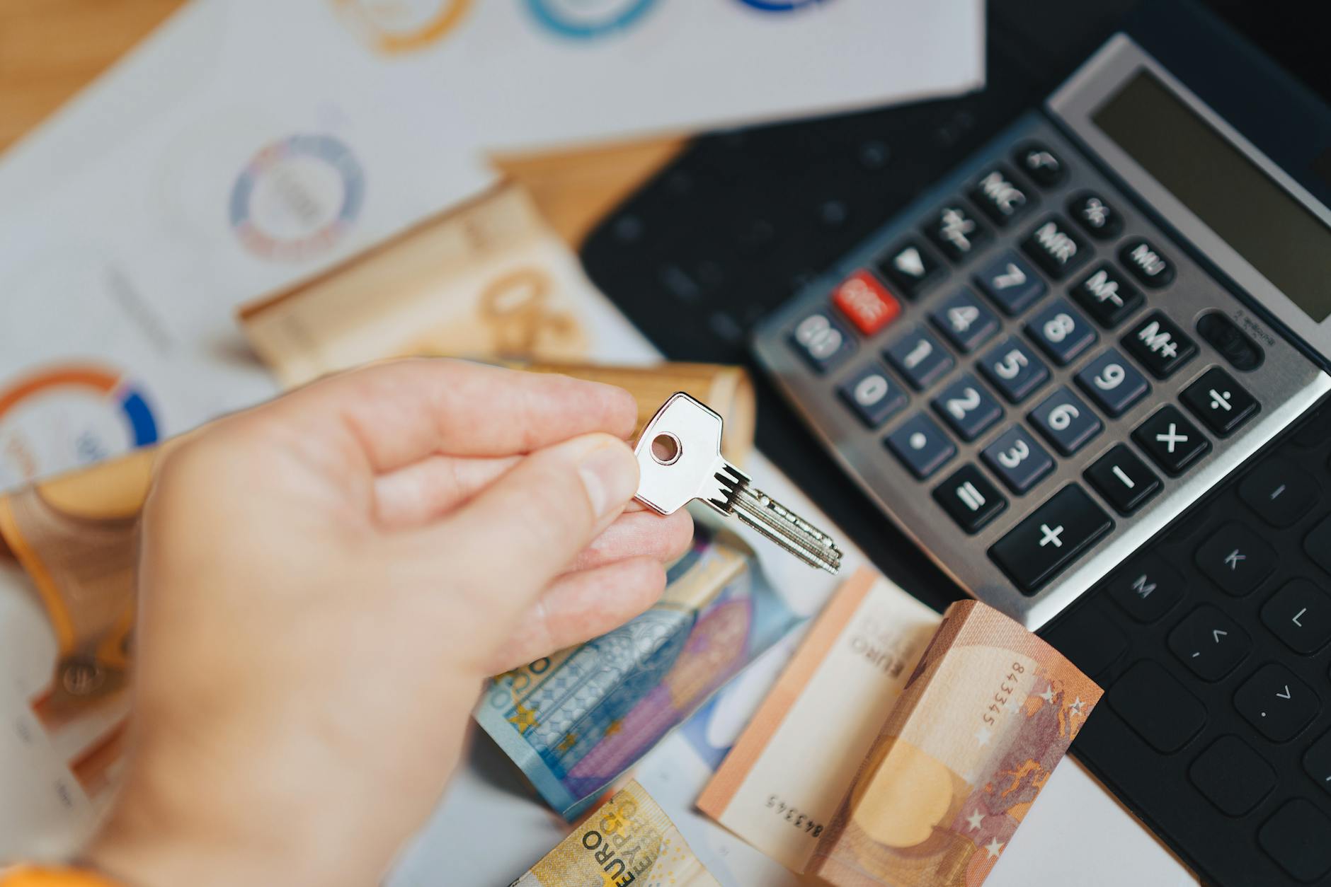 Dłoń z kluczem nad banknotami euro i kalkulatorem, symbol pożyczki