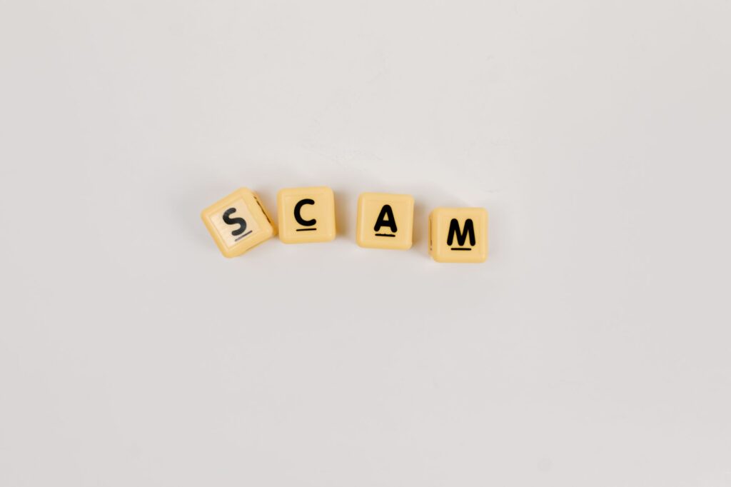 Kostki Scrabble układające słowo SCAM na jasnym tle