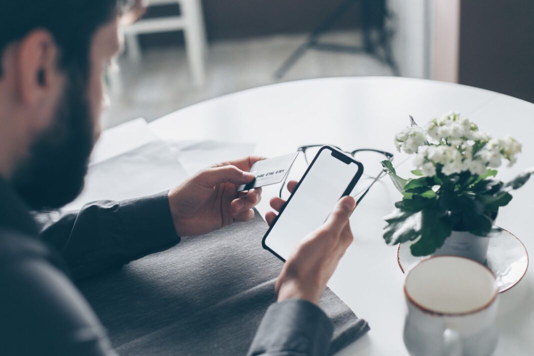 Mężczyzna trzymający kartę płatniczą i smartfon przy stole Mężczyzna trzymający kartę płatniczą i smartfon przy stole