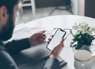 Co zrobić, gdy ktoś dzwoni i prosi o kod do aplikacji bankowej? Mężczyzna trzymający kartę płatniczą i smartfon przy stole